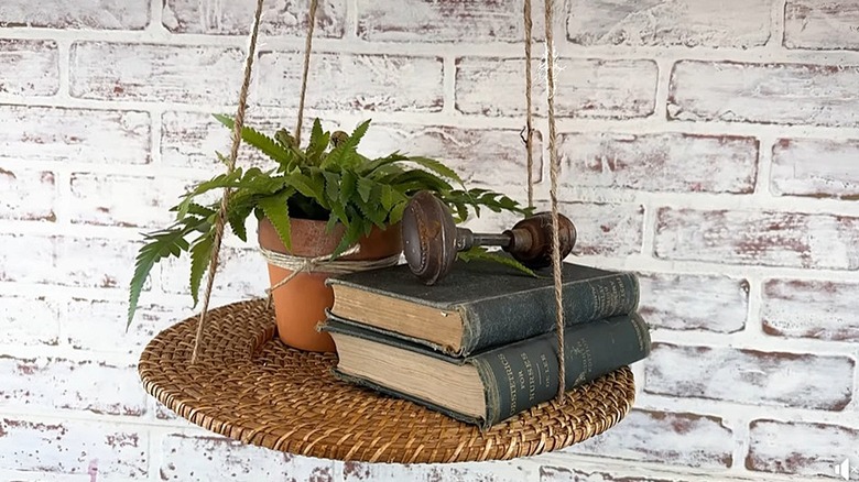 Hanging shelf made from a wicker charger with books and a plant on it