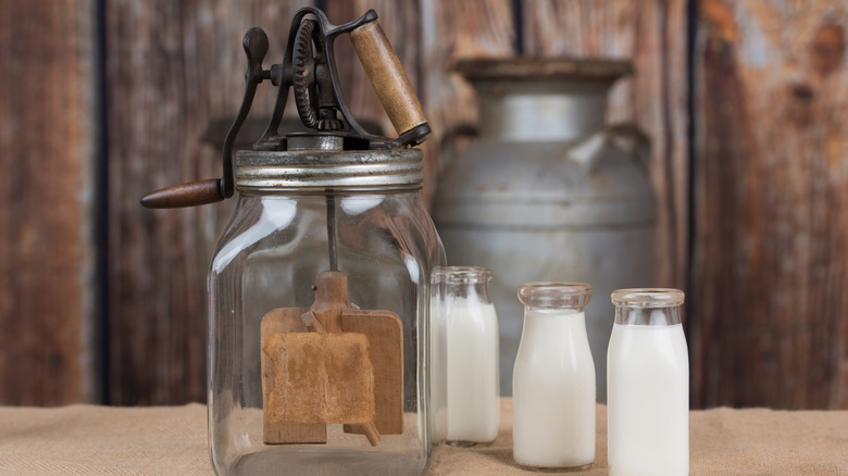 Hand-crank butter churn with milk bottles and cans in the background