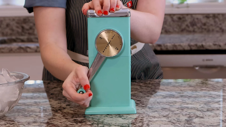 Person operating a vintage teal manual ice crusher