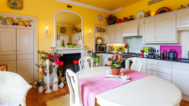A kitchen with yellow walls, white cabinetry and built-ins with stencil art, and a white table with matching chairs.