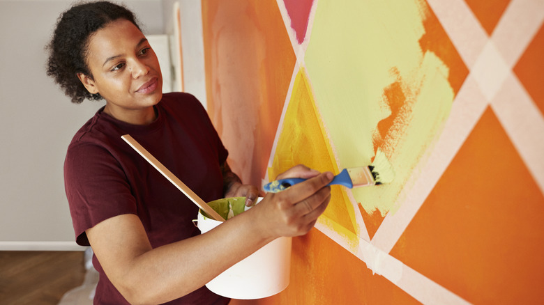 Woman painting orange and yellow geometric pattern on a wall