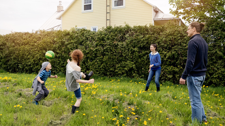 Dad and three kids kicking a ball in yard with flowers
