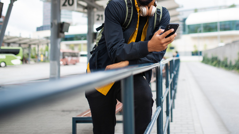 Man holding phone is waiting on a sidewalk