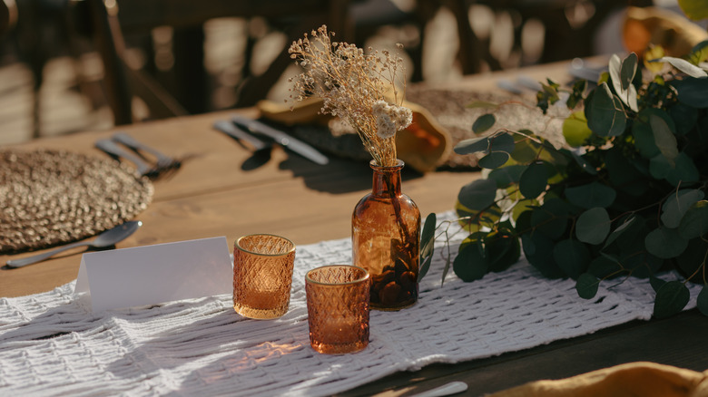 Amber glassware on a white runner on a wooden table with leaves and branches as fall decor