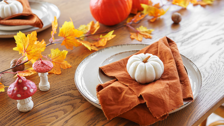 Orange napkins on white plates with pumpkin, chestnuts, and leaves as table decor