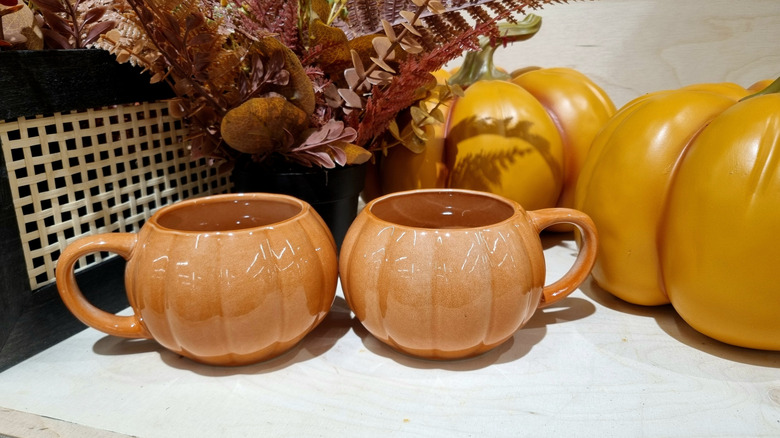 Pumpkin-shaped mugs that are part of a fall display