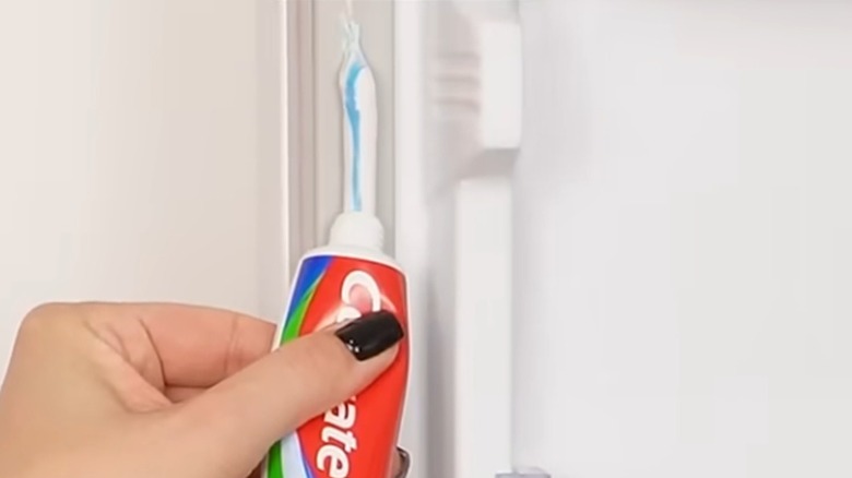 Person spreads toothpaste along refrigerator seal