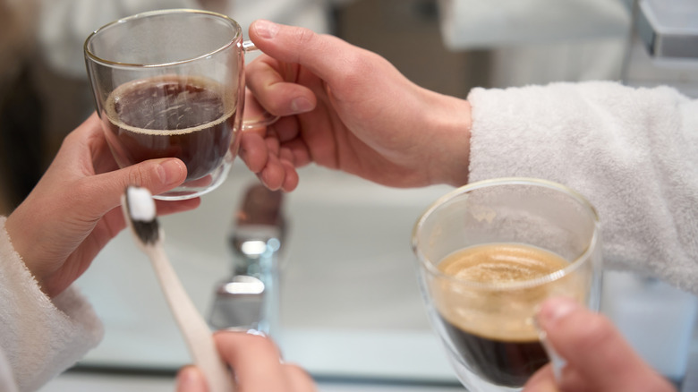 A person holds a toothbrush by a coffee mug