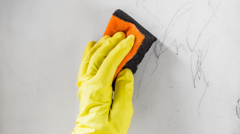 A person cleans crayon drawings on wall