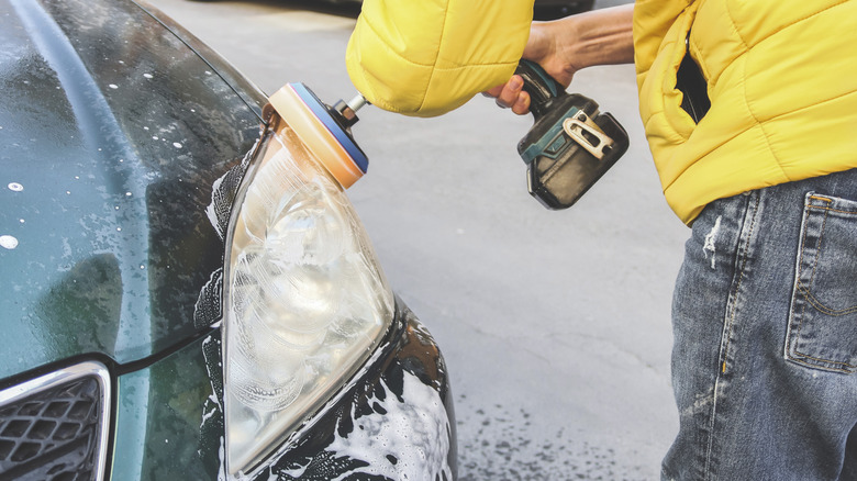 Person using a drill attachment to polish headlight on a car