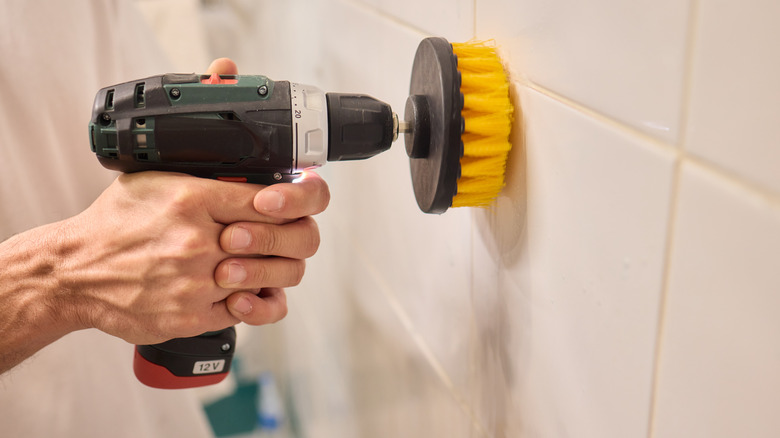 Person using a drill with a yellow scrub brush attachment to clean tile shower surround