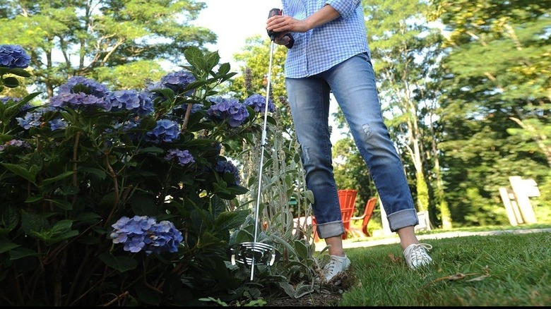 Person working in a flower garden using the DrillTill attachment on a power drill