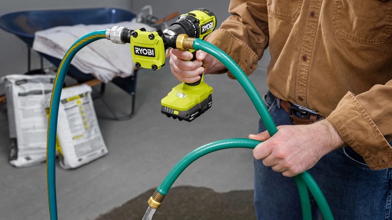 Man using the Ryobi hex shank drill pump attached to a Ryobi drill and a garden hose