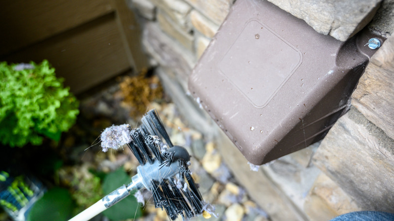 Dryer vent cleaning brush attachment for drill next to an exterior dryer vent