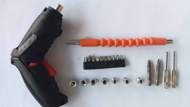 Power drill laying on a white table with various accessories, including an orange flexible shaft bit holder