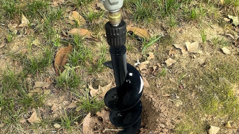Black garden auger attachment for drill creating a hole in the soil