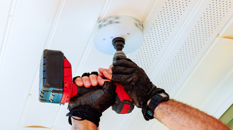 Person wearing gloves and using a drill fitted with a hole saw attachment making a hole in a ceiling