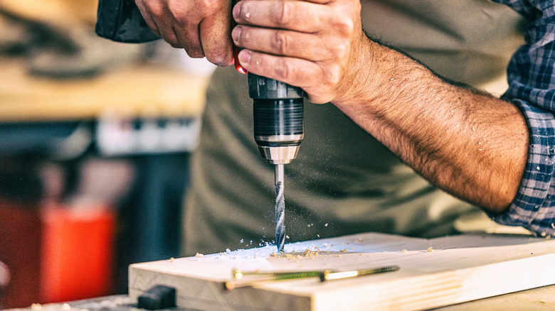 Person using a power drill to make a hole in a piece of wood