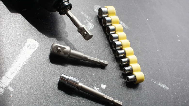 Drill laying on a black work surface with a socket adapter attachment and various sockets