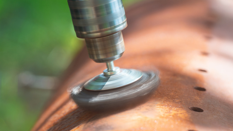 Wire brush drill attachment being used to remove rust from old metal