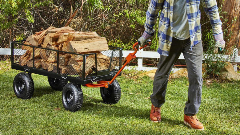 A man pulling a utility cart full of wood.