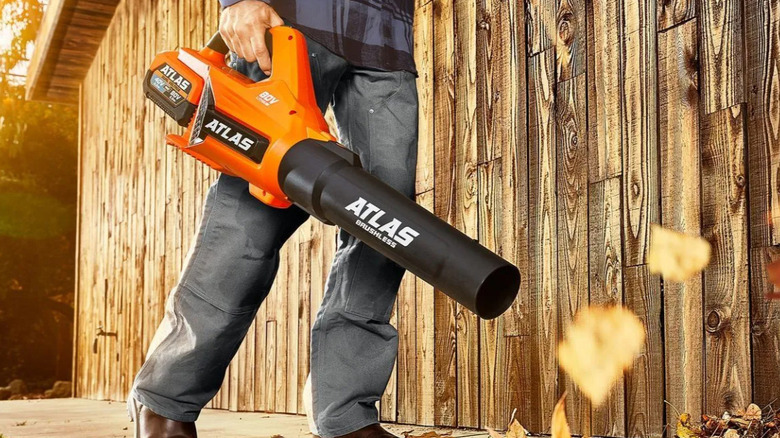 A man blowing leaves with an orange leaf blower.