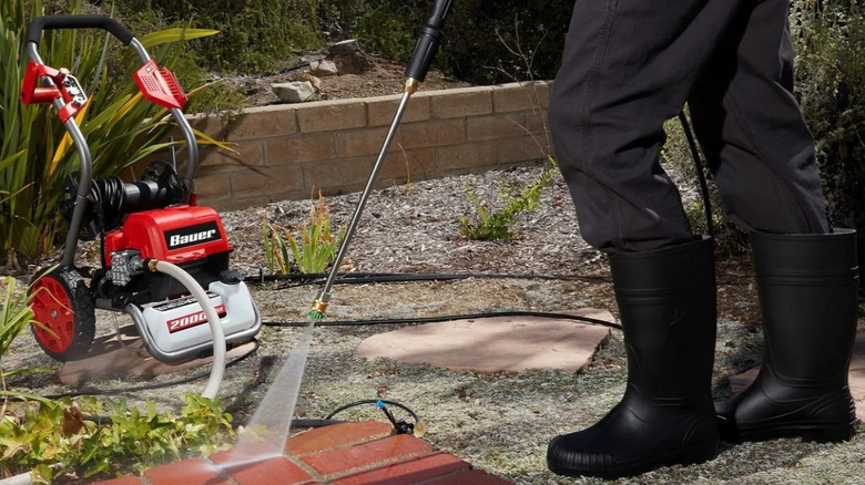 A man spraying a brick patio with the BAUER pressure washer.