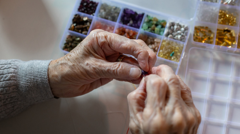 Hands threading a bead onto a string with a divided container of colorful beads in the background