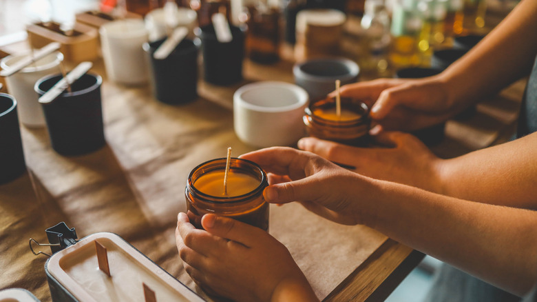 Two people making jar candles at a table with several other homemade candles in the background