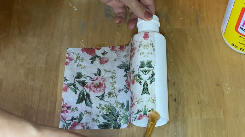 Woman brushing decoupage glue onto a patterned paper that she's decoupaging to a bottle