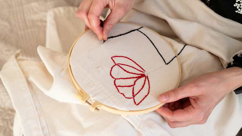 A person embroidering a floral design on fabric held in an embroidery hoop