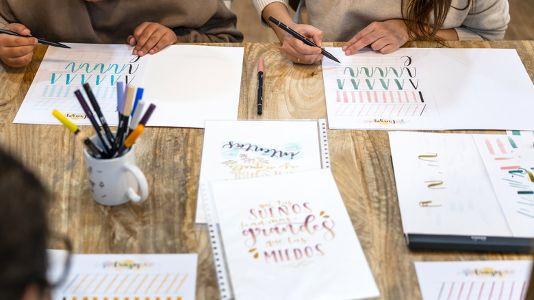 People learning how to do hand lettering with markers and practice papers on the table