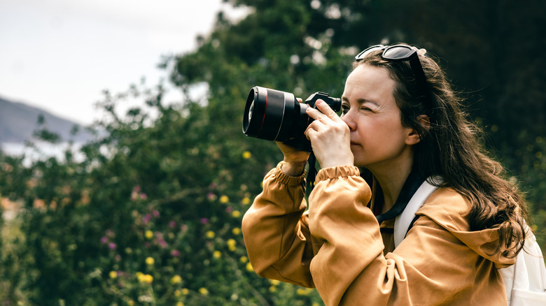 Woman in a jacket taking a photo with a professional camera in front of a tree