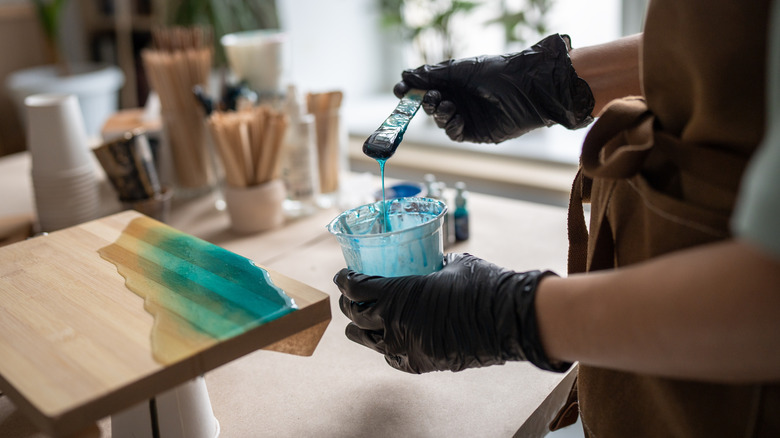 Person holding a container of resin and applying it to a piece of wood