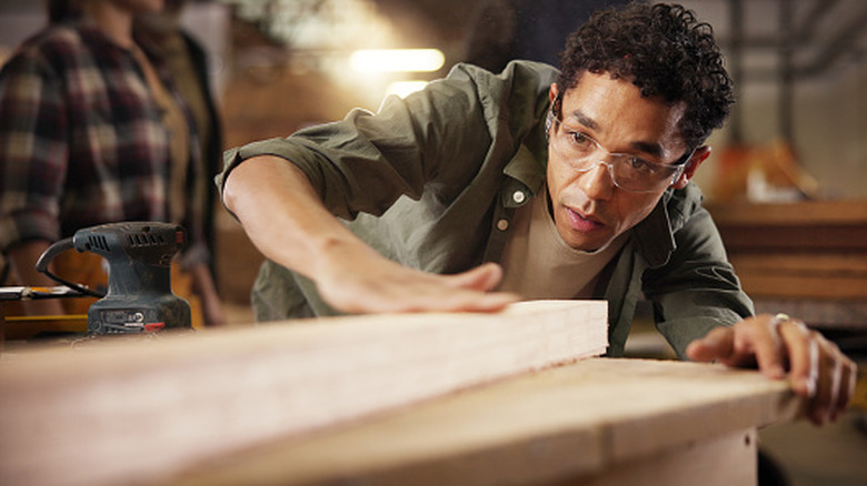 Man leaning over looking at a board and feeling it with his hand