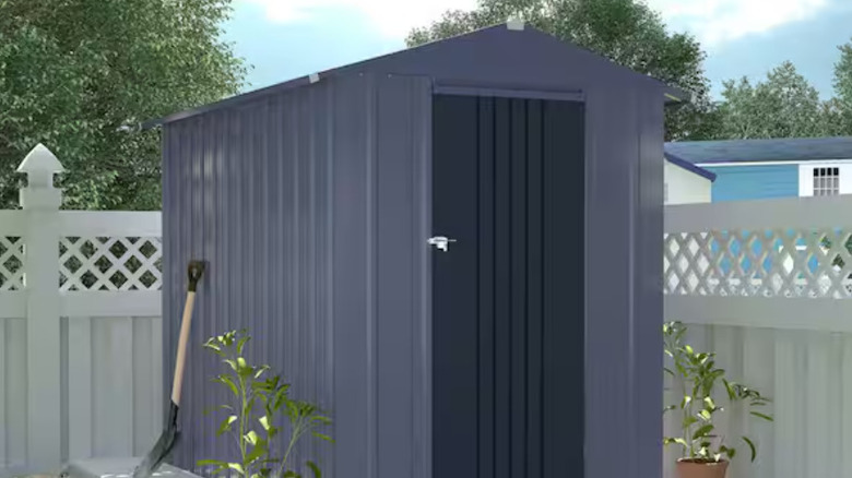 The VEIKOUS gray shed outdoors next to a fence.