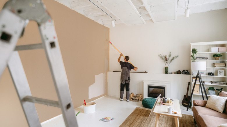 A person in coveralls painting an accent wall in a living room