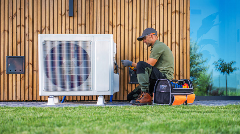 Technician in a vest works on an air unit outside a house