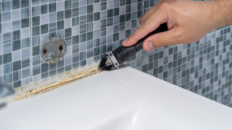 Person using a silicone caulk and grout scraper on tile