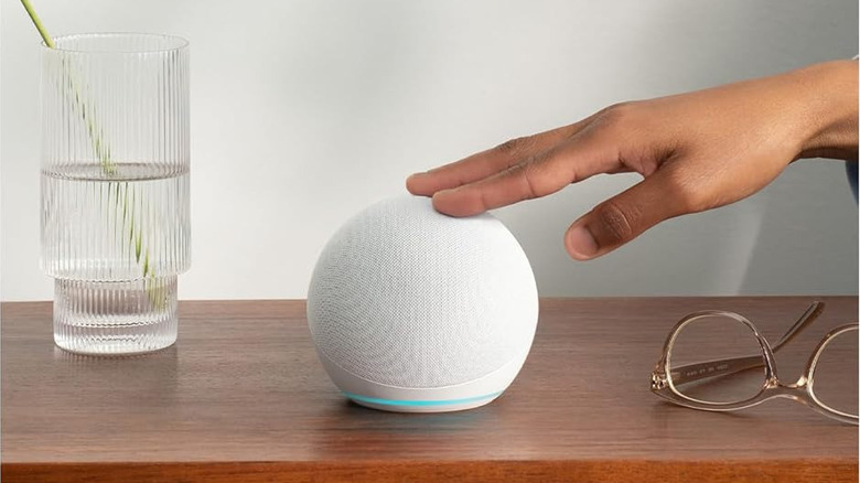 Woman tapping smart AI-powered Amazon Echo on wood table beside water and glasses