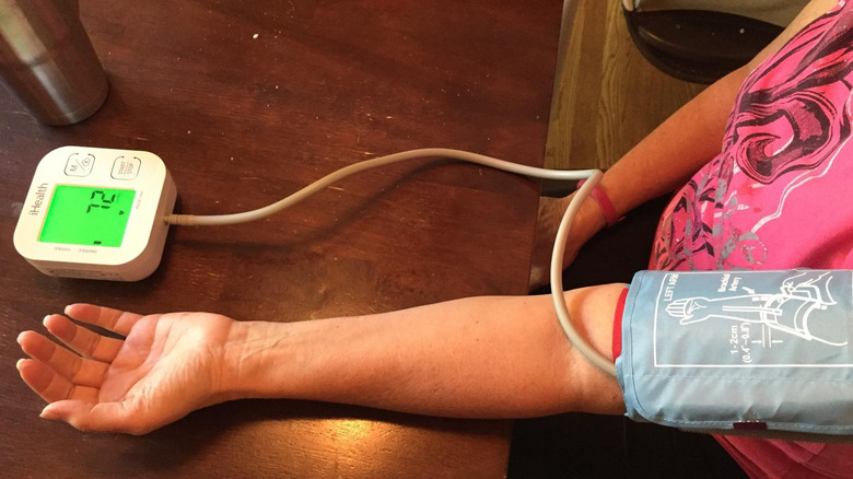 Woman monitoring blood pressure via a smart health monitor on hardwood table