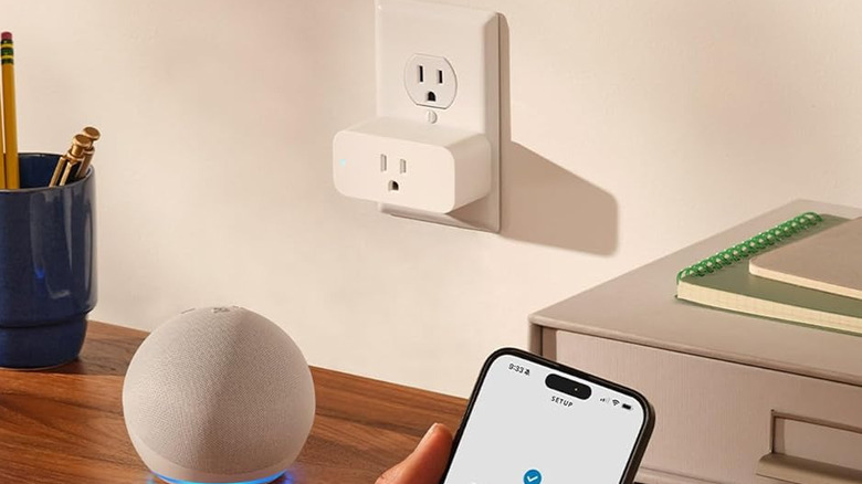 Smart home plug behind Amazon Echo and smartphone with app powered on