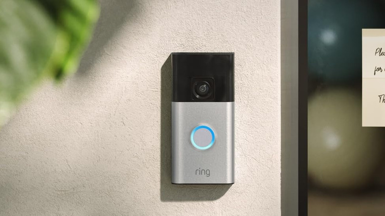 Ring doorbell and security camera attached to exterior wall beside plant and glass window