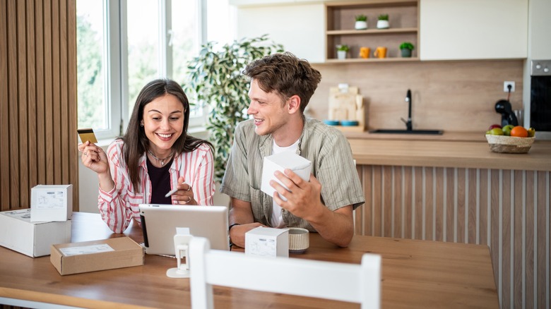 Smiling young couple unboxing gifts in kitchen with tablet