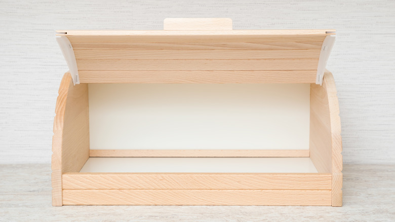 An opened wooden breadbox, empty, against a white wall