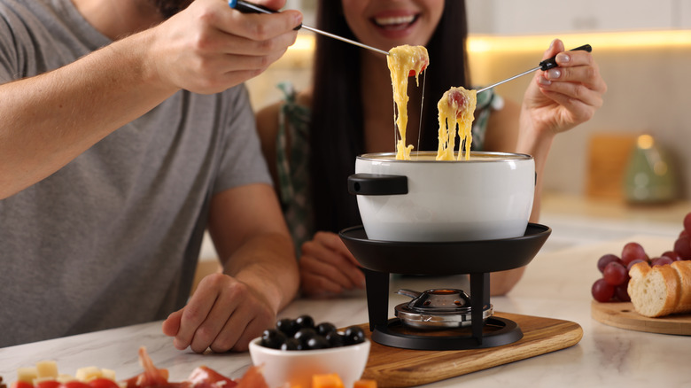 A couple eats out of a fondue pot on a stand using skewers