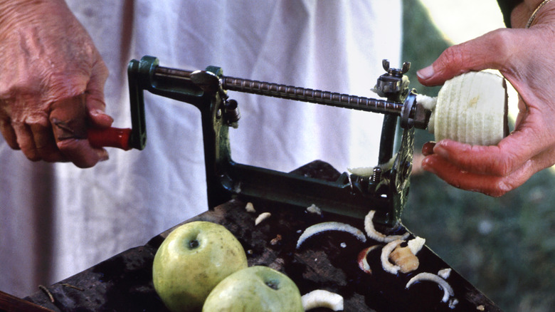 A person uses a vintage hand-crank apple peeler to peel an apple