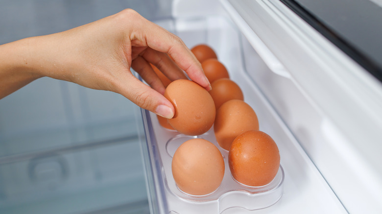 Person putting brown eggs into a plastic egg holder in the fridge