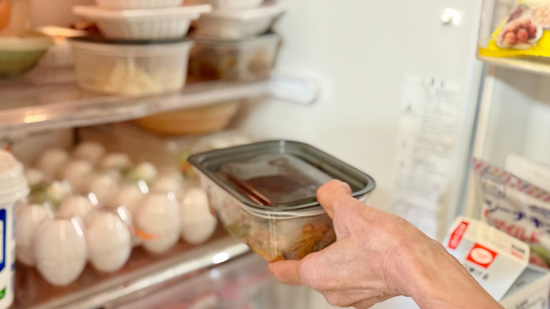 Person putting a container of leftovers on the top shelf in the refrigerator