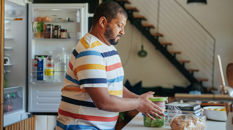 Man organizing food on counter with refrigerator open behind him